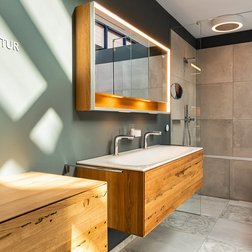 Ein modernes Badezimmer mit eleganten Holzschränken und einem großen Spiegel, der sanft beleuchtet ist.