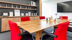 Ein moderner Besprechungsraum mit einem großen Holztisch und roten Stühlen, ideal für Teammeetings und Präsentationen.