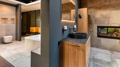 Das Badezimmer zeigt eine stilvolle Kombination aus Holz und Stein, mit einem freistehenden Bad und einem großen Spiegel.