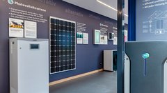 Ein moderner Ausstellungsraum zeigt verschiedene Photovoltaiksysteme und Energiespeicherlösungen an einer blauen Wand.