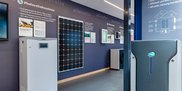 Ein moderner Ausstellungsraum zeigt verschiedene Photovoltaiksysteme und Energiespeicherlösungen an einer blauen Wand.