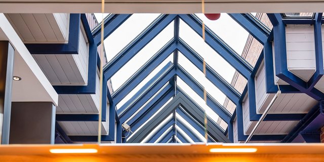 Ein Blick auf die moderne Architektur mit blauen Balken und einem lichtdurchfluteten Dach, das eine offene Atmosphäre schafft.