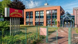 Ein modernes Gebäude mit großen Fenstern und einem auffälligen roten Schild, das Dienstleistungen im Sanitärbereich anbietet.