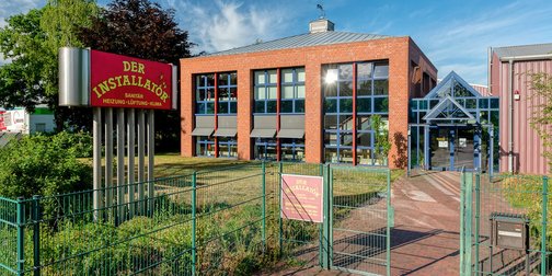 Ein modernes Gebäude mit großen Fenstern und einem auffälligen roten Schild, das Dienstleistungen im Sanitärbereich anbietet.