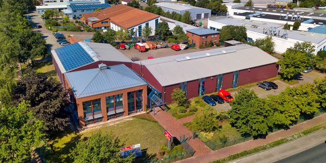 Ein modernes Gebäude mit roten Wänden und großen Fenstern, umgeben von Bäumen und einem Parkplatz mit mehreren Autos.