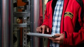 Ein Techniker in einer roten Jacke bedient ein Tablet, während er in einer industriellen Umgebung arbeitet.