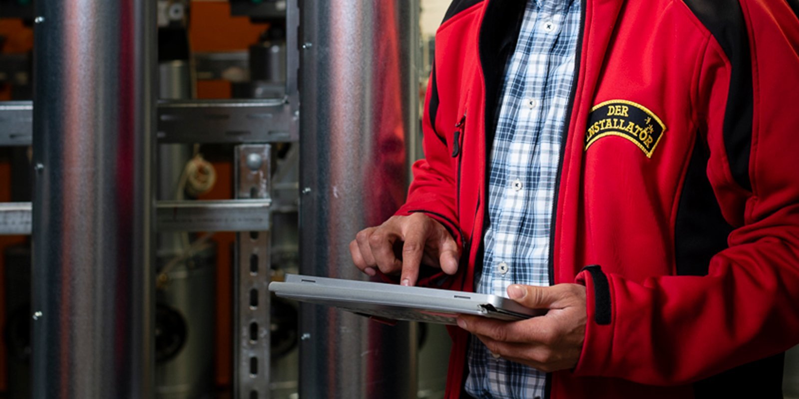 Ein Techniker in einer roten Jacke bedient ein Tablet, während er in einer industriellen Umgebung arbeitet.