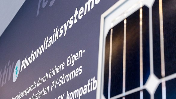 Ein modernes Solarpanel ist an einer Wand montiert, umgeben von informativen Texten über Photovoltaiksysteme.