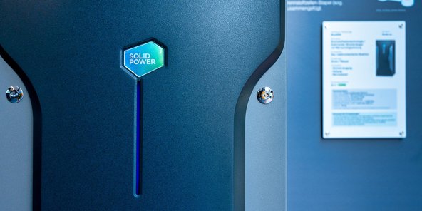 Ein modernes Gerät mit dem Schriftzug 'SOLID POWER' auf einer blauen Oberfläche, das in einem Ausstellungsraum präsentiert wird.