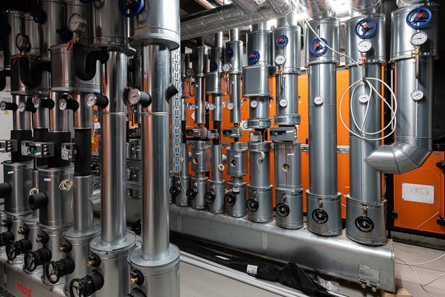 Eine komplexe Anordnung von silbernen Rohren und Ventilen, die in einem industriellen Raum installiert sind, mit orangefarbenen Wänden.