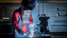 Ein Schweißer arbeitet konzentriert in einer dunklen Werkstatt, während Funken und Licht aus dem Schweißgerät sprühen.