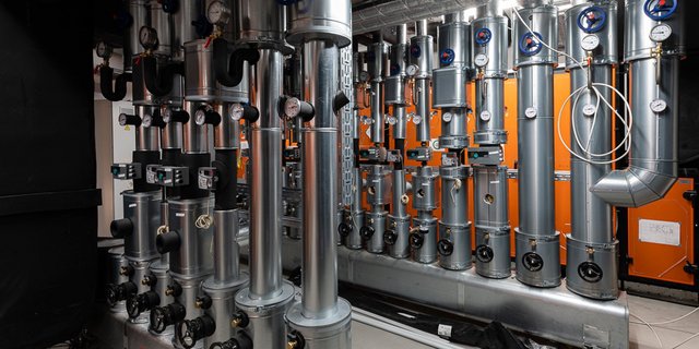 Eine komplexe Anordnung von silbernen Rohren und Ventilen, die in einem technischen Raum installiert sind, mit orangefarbenen Wänden im Hintergrund.