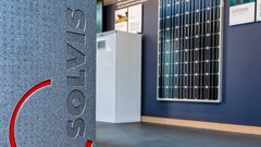 Ein graues Gerät mit dem Logo 'SOLVIS' steht im Vordergrund, während ein Solarpanel an der Wand sichtbar ist.